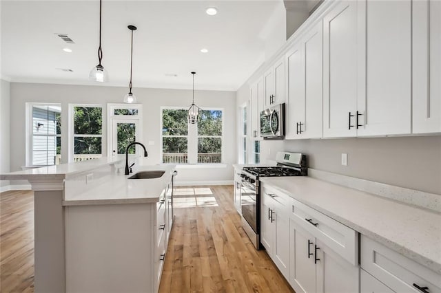 kitchen with appliances with stainless steel finishes, decorative light fixtures, sink, light hardwood / wood-style floors, and white cabinets