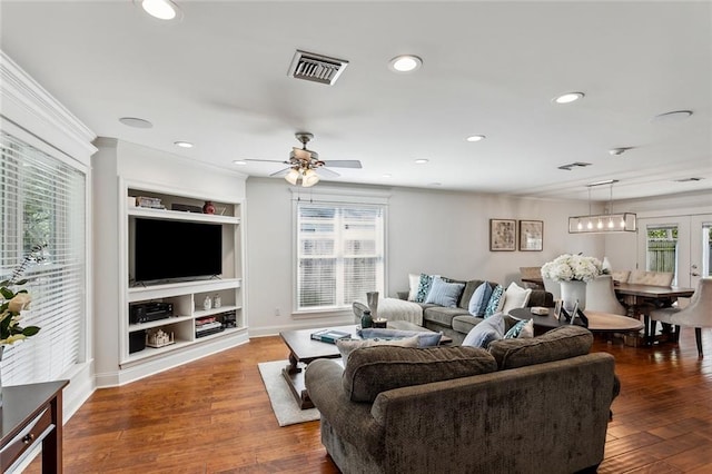 living room featuring built in shelves, dark hardwood / wood-style floors, ceiling fan, and crown molding