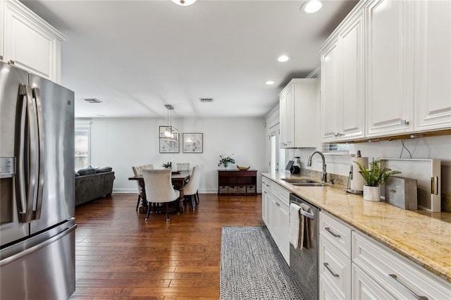 kitchen featuring sink, appliances with stainless steel finishes, hanging light fixtures, white cabinets, and dark wood-type flooring