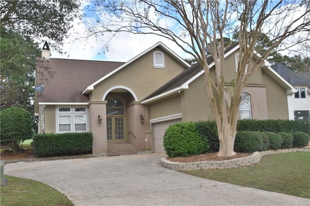 view of front of home featuring a garage, driveway, brick siding, and stucco siding