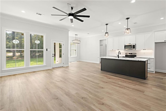 kitchen featuring light wood-type flooring, stainless steel appliances, pendant lighting, a center island with sink, and white cabinetry