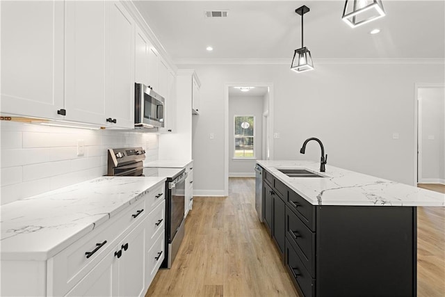 kitchen with stainless steel appliances, decorative light fixtures, white cabinets, light hardwood / wood-style floors, and an island with sink