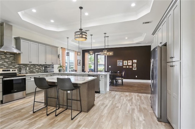 kitchen featuring stainless steel appliances, a kitchen island, a kitchen breakfast bar, a tray ceiling, and wall chimney exhaust hood