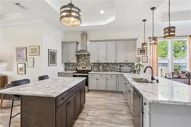 kitchen featuring stainless steel appliances, sink, a kitchen breakfast bar, wall chimney exhaust hood, and hanging light fixtures