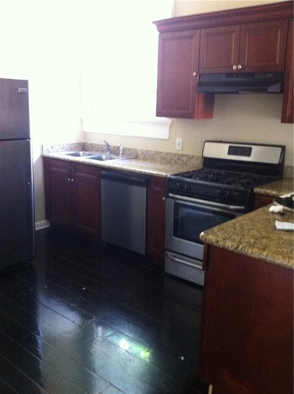 kitchen featuring stainless steel appliances, sink, light stone counters, and dark hardwood / wood-style flooring