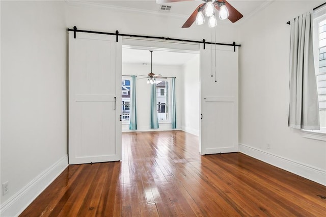 spare room featuring dark hardwood / wood-style flooring, a barn door, crown molding, and ceiling fan