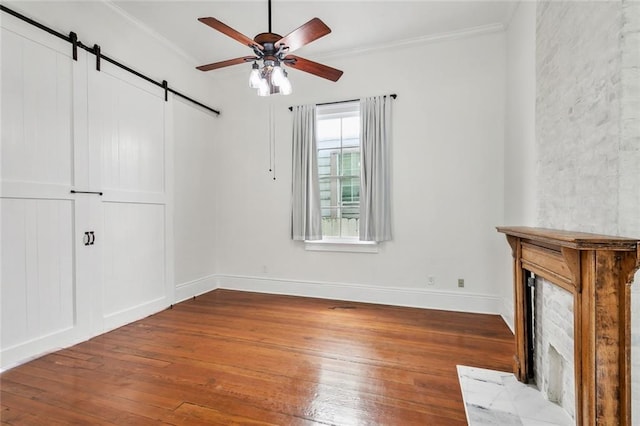 interior space with ornamental molding, wood-type flooring, a barn door, and ceiling fan