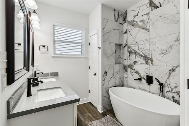 full bathroom with double vanity, a soaking tub, wood finished floors, and a sink