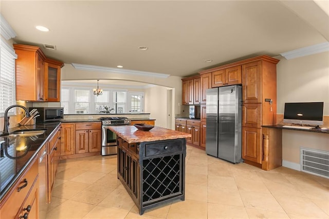 kitchen with dark stone counters, ornamental molding, stainless steel appliances, sink, and a kitchen island