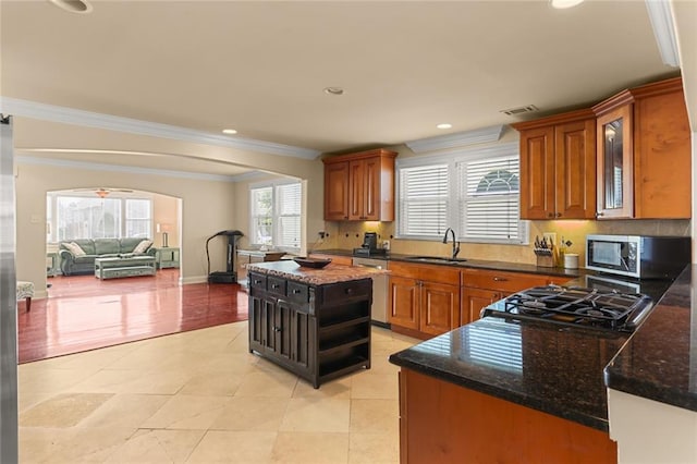 kitchen with dark stone counters, stainless steel appliances, a kitchen island, and crown molding