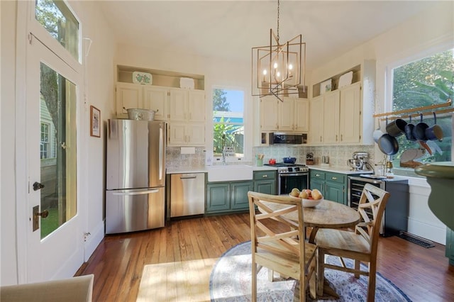 kitchen with stainless steel appliances, green cabinetry, hanging light fixtures, light hardwood / wood-style flooring, and decorative backsplash