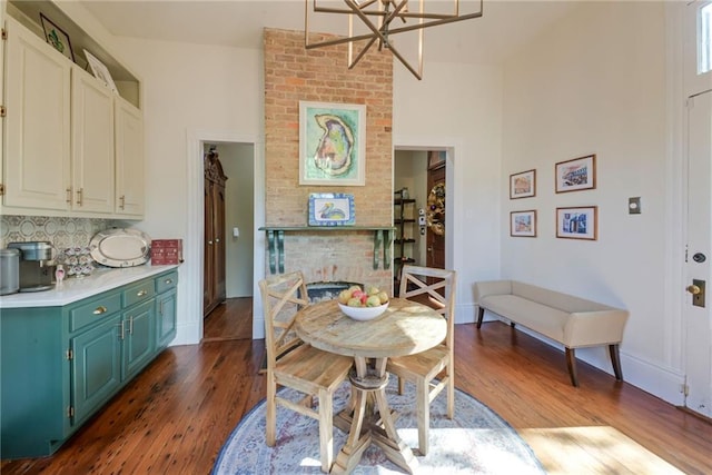 dining space with dark wood-type flooring, a notable chandelier, and a brick fireplace