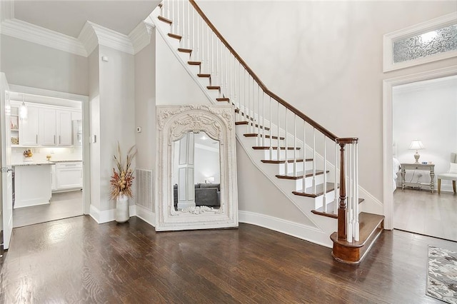 entrance foyer with dark wood-type flooring, a towering ceiling, and ornamental molding