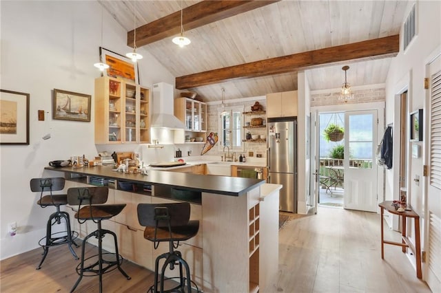 kitchen with a kitchen bar, decorative light fixtures, stainless steel fridge, kitchen peninsula, and wall chimney range hood