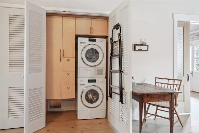 laundry area featuring cabinets, stacked washer / drying machine, and light hardwood / wood-style floors