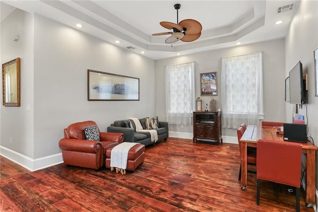 living area with hardwood / wood-style flooring, ceiling fan, and a tray ceiling