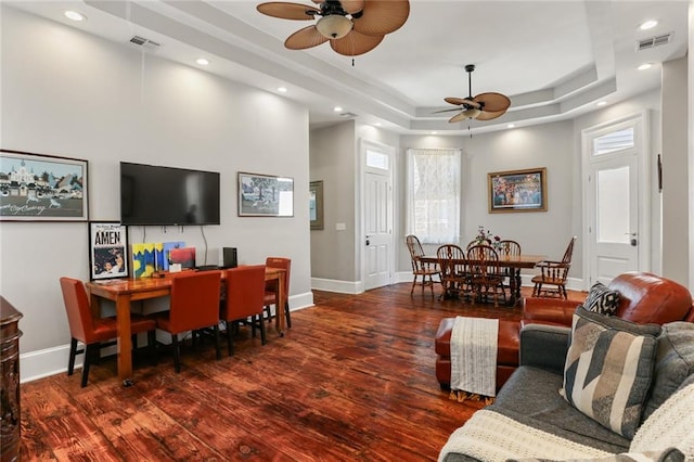 living room featuring a wealth of natural light, a raised ceiling, ceiling fan, and dark wood-type flooring