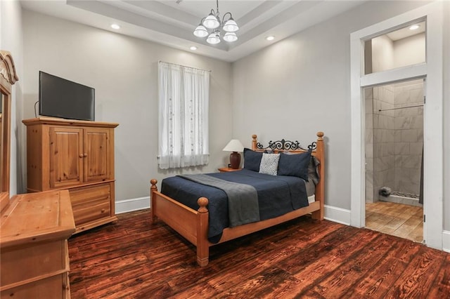 bedroom featuring a raised ceiling, ensuite bath, dark hardwood / wood-style flooring, and an inviting chandelier