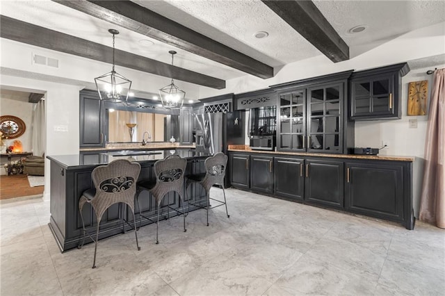 kitchen featuring hanging light fixtures, a textured ceiling, a notable chandelier, a breakfast bar area, and beamed ceiling