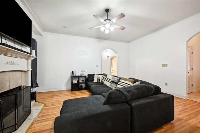 living room featuring ceiling fan, light hardwood / wood-style floors, ornamental molding, and a fireplace