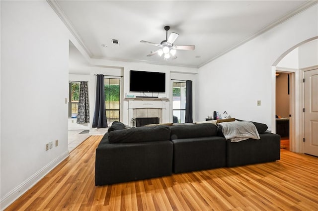 living room with ceiling fan, light hardwood / wood-style floors, crown molding, and a tiled fireplace