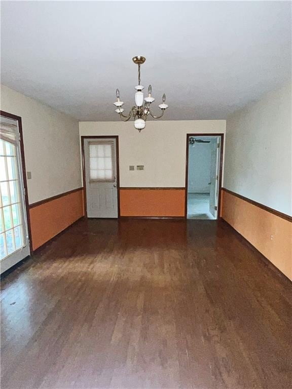 spare room with dark wood-type flooring, wooden walls, and a chandelier