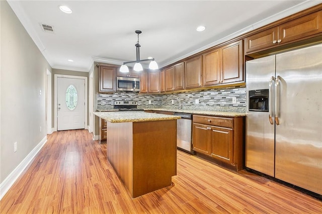 kitchen featuring stainless steel appliances, a kitchen island, light wood-type flooring, light stone countertops, and hanging light fixtures