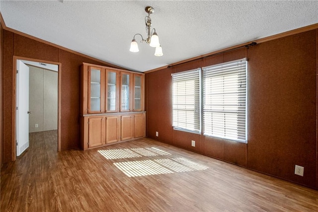 unfurnished dining area with crown molding, wood walls, a chandelier, lofted ceiling, and light hardwood / wood-style floors