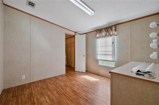 interior space featuring a textured ceiling, light hardwood / wood-style floors, and crown molding