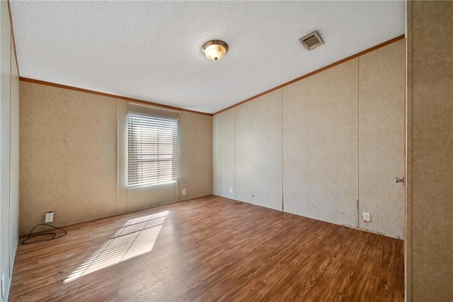 empty room featuring crown molding, wood-type flooring, and a textured ceiling