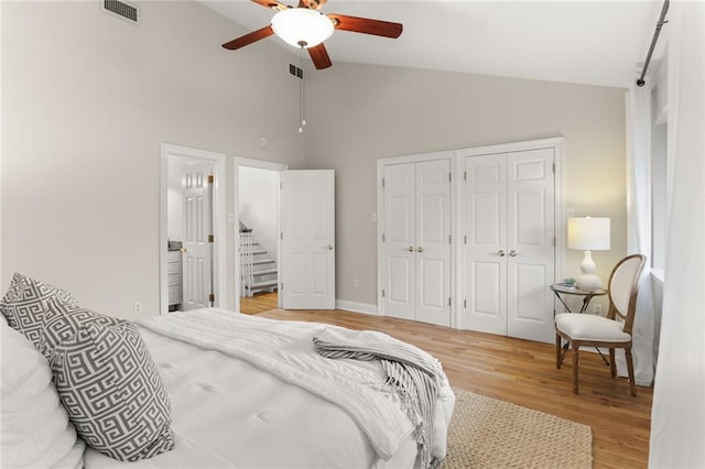 bedroom featuring ensuite bath, light wood-type flooring, high vaulted ceiling, two closets, and ceiling fan