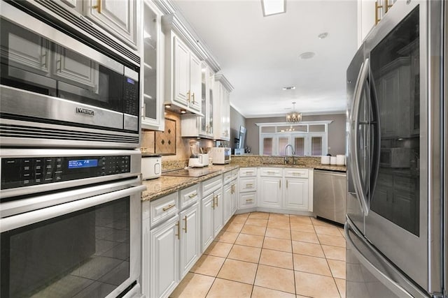 kitchen with stainless steel appliances, sink, light tile patterned floors, a notable chandelier, and white cabinets