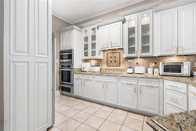 kitchen featuring tasteful backsplash, light tile patterned flooring, crown molding, white cabinetry, and stainless steel microwave