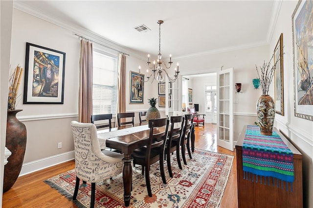 dining space with hardwood / wood-style floors, crown molding, an inviting chandelier, and french doors