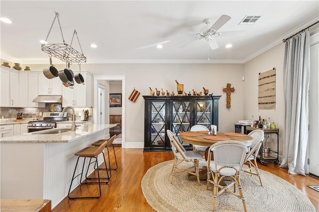 dining area featuring ornamental molding, light wood-type flooring, sink, and ceiling fan