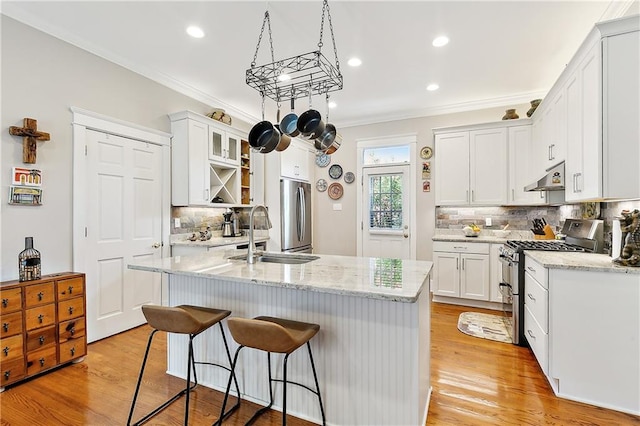 kitchen with crown molding, appliances with stainless steel finishes, an island with sink, white cabinets, and light hardwood / wood-style flooring