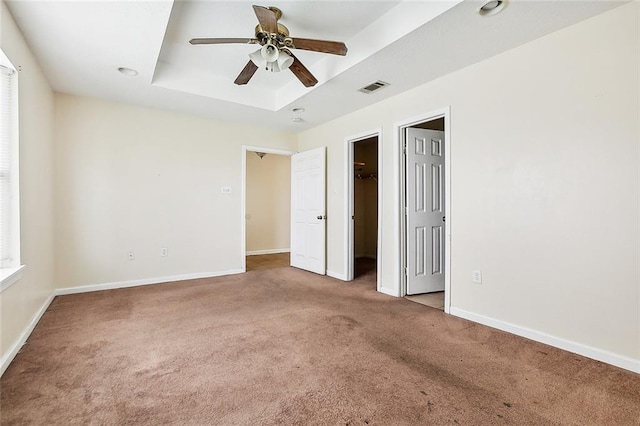 unfurnished bedroom with ceiling fan, carpet, and a tray ceiling