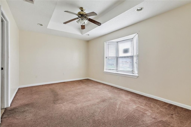 carpeted empty room with ceiling fan and a raised ceiling