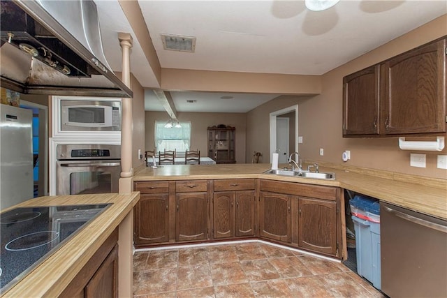 kitchen with butcher block countertops, wall chimney range hood, appliances with stainless steel finishes, and sink