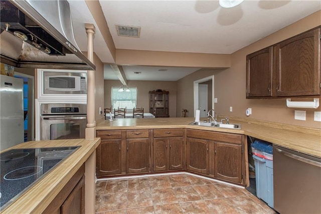 kitchen with appliances with stainless steel finishes, a sink, light countertops, and a peninsula