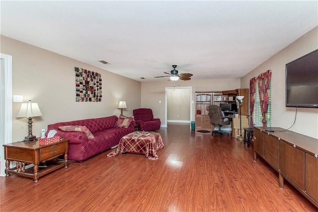 living room featuring light wood finished floors, a ceiling fan, and a desk