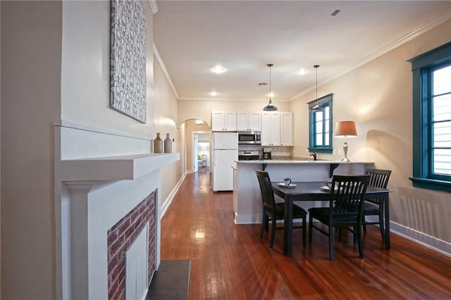 dining area featuring dark hardwood / wood-style floors, a brick fireplace, crown molding, and sink