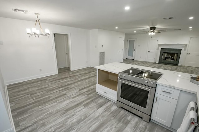 kitchen with white cabinets, light wood-type flooring, light stone counters, and electric range