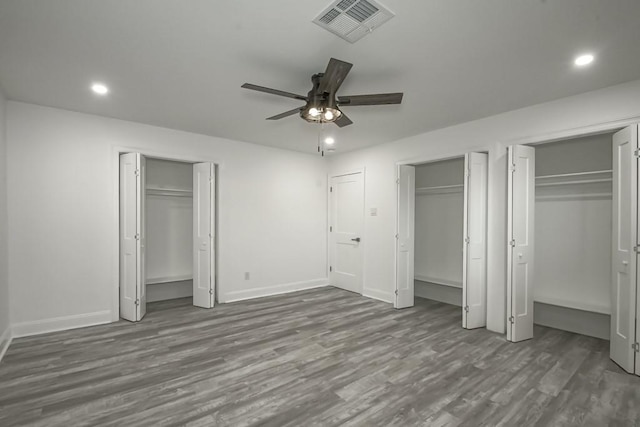 unfurnished bedroom with hardwood / wood-style floors, two closets, and ceiling fan