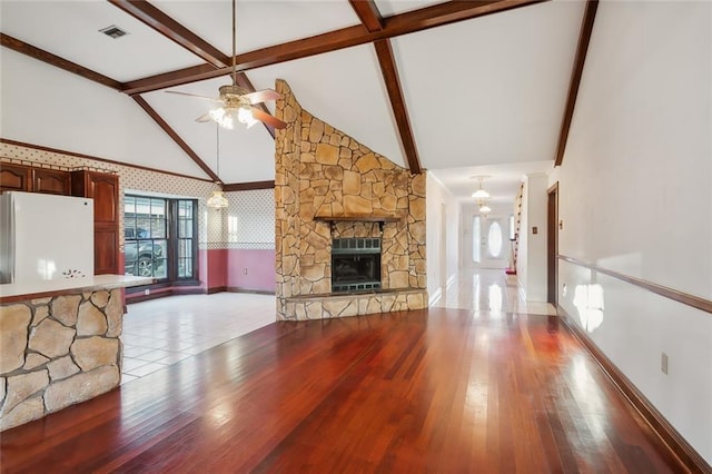 unfurnished living room with a stone fireplace, high vaulted ceiling, beamed ceiling, ceiling fan, and light wood-type flooring