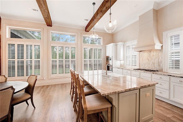 kitchen with custom exhaust hood, decorative light fixtures, light stone countertops, a kitchen island with sink, and stainless steel appliances