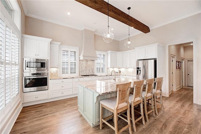 kitchen with premium range hood, tasteful backsplash, white cabinetry, a center island with sink, and stainless steel appliances