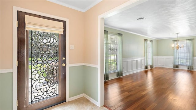 entryway featuring wood finished floors, wainscoting, a chandelier, ornamental molding, and visible vents