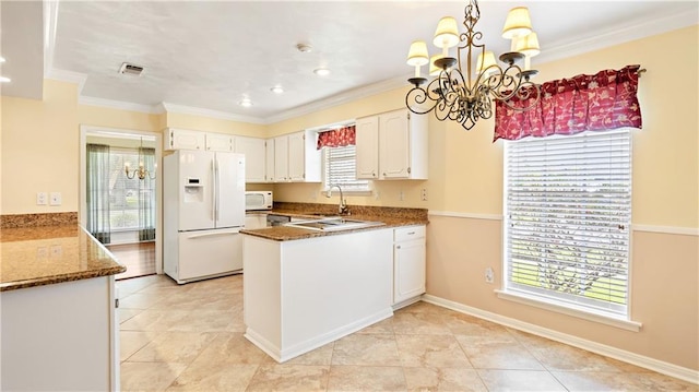 kitchen with white cabinets, a peninsula, a notable chandelier, white appliances, and crown molding