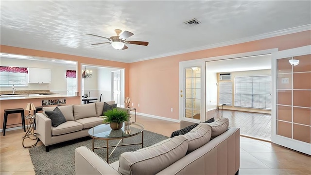 living area with baseboards, visible vents, a ceiling fan, crown molding, and light tile patterned floors